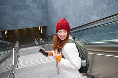 Portrait of young woman standing against escalator