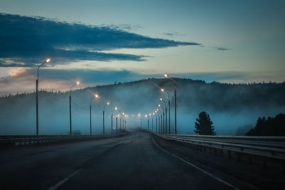 Empty road leading towards silhouette mountains in foggy weather