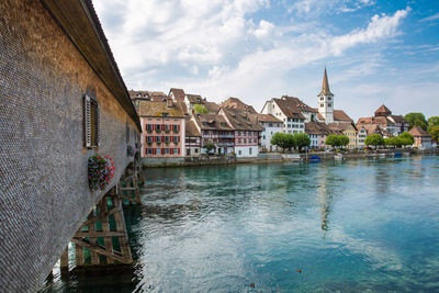 View of buildings at waterfront against cloudy sky