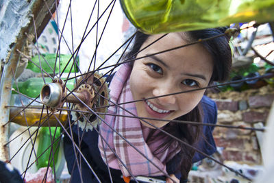 Portrait of smiling young woman seen through bicycle wheel