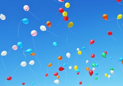 Low angle view of balloons flying against blue sky