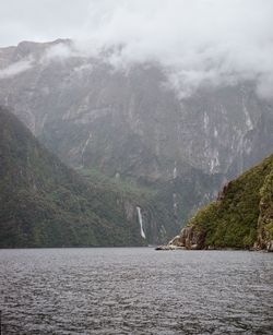 Scenic view of water and mountains against a gray sky in the milford sounds.
