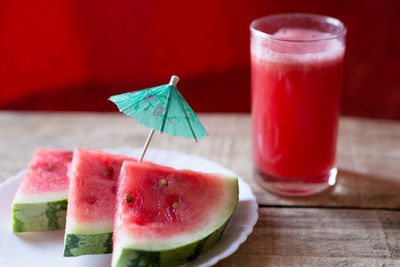 Close-up of watermelon slices in plate by blended drink on table
