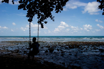 Rear view of silhouette boy swinging at beach