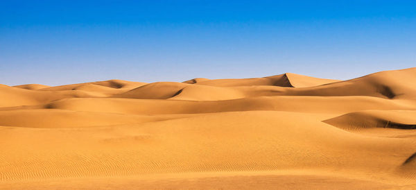 Sand dunes in desert against clear blue sky