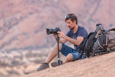 Man photographing while sitting on rock