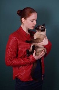 Young woman holding siamese cat against gray background