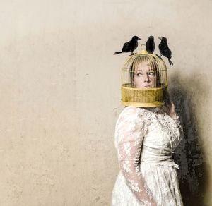 Woman wearing cage on head standing against wall