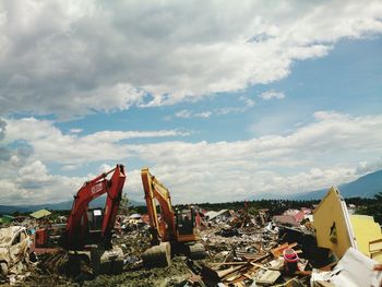 Vehicles at dumping ground against cloudy sky