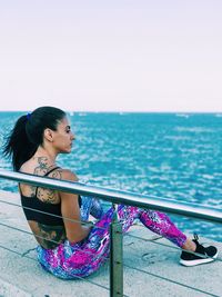 Woman sitting by railing against sea