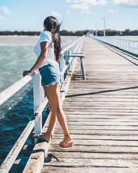 Rear view of woman standing on pier against sky