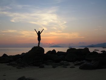 Silhouette man on rock at beach against sky during sunset