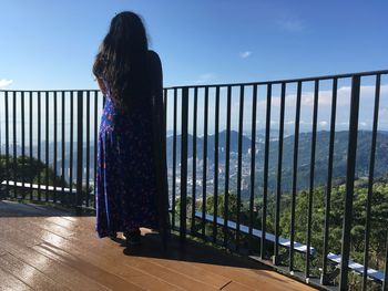 Rear view of woman standing by railing against sky