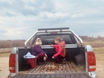 Rear view of women sitting on road against sky