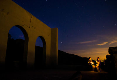 Tourists by old ruins at night against sky