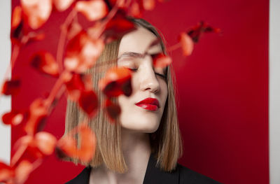 Beautiful blond woman with eyes closed behind twig against red background