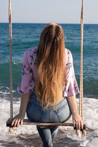 Young woman with long hair sitting on the swing on the beach and enjoying the view.