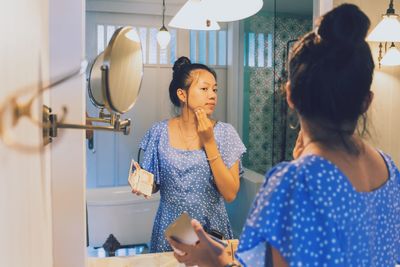 Woman applying make-up while standing in front of mirror