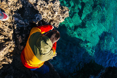 High angle view of man sitting on rock formation by sea