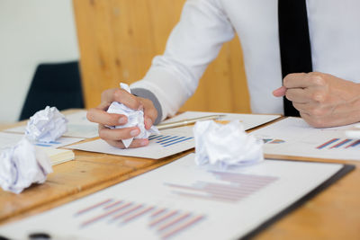 Midsection of businessman holding crumpled paper on table