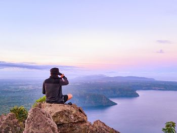 Rear view of man photographing rock in sea against sky