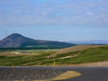 Scenic view of road by field against sky