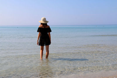 Rear view of man standing on beach against clear sky