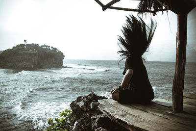 Side view of woman tossing hair while sitting by sea against sky