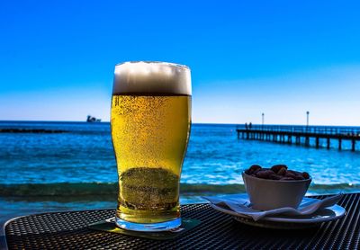 Close-up of beer glass and nuts in bowl on table against sea