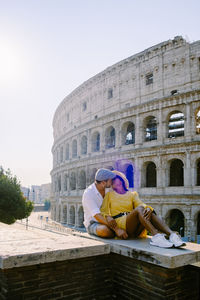 Woman sitting at historical building against sky