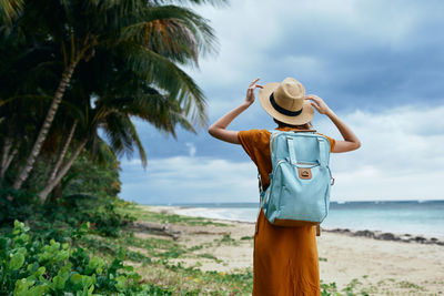 Rear view of woman standing at beach against sky