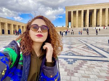 Portrait of young woman wearing sunglasses standing under the sky 