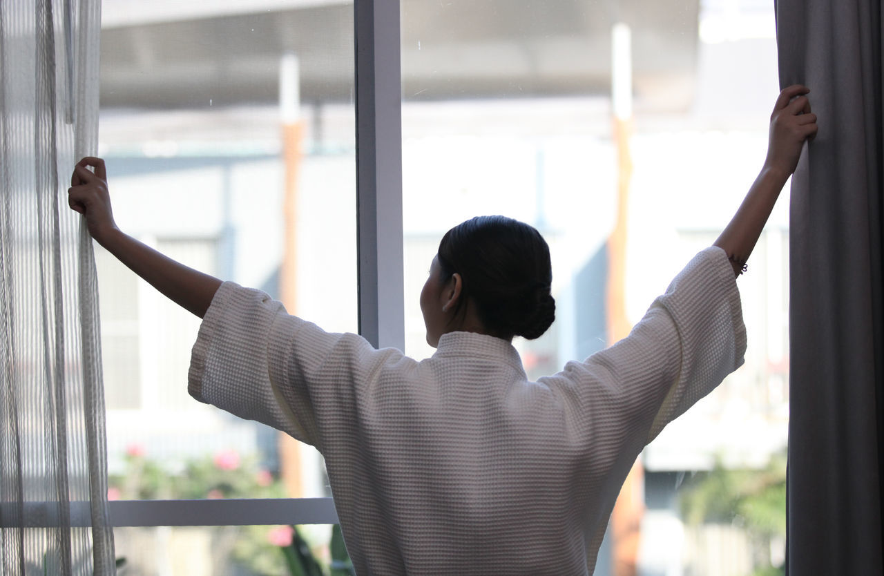 REAR VIEW OF A YOUNG MAN LOOKING THROUGH WINDOW