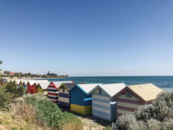 Beach huts by sea against clear blue sky