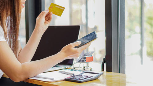 Midsection of woman holding smart phone by window