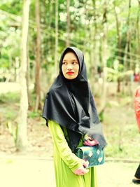 Young woman wearing hijab looking away while standing against trees in forest