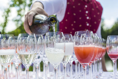 Midsection of bartender pouring aperitif in champagne flutes on table during outdoor party