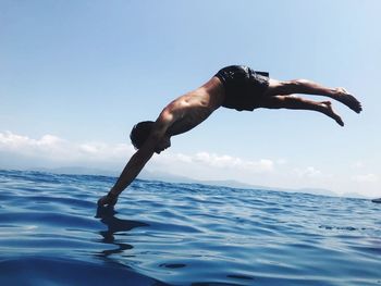 Full length of shirtless man in sea against sky