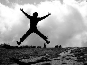 Rear view of silhouette man jumping on field against sky