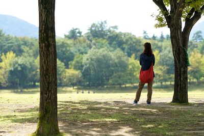 Rear view of woman standing on tree trunk