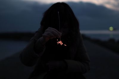 Woman holding sparklers while standing on pier at dusk