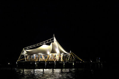 Illuminated bridge over river against clear sky at night