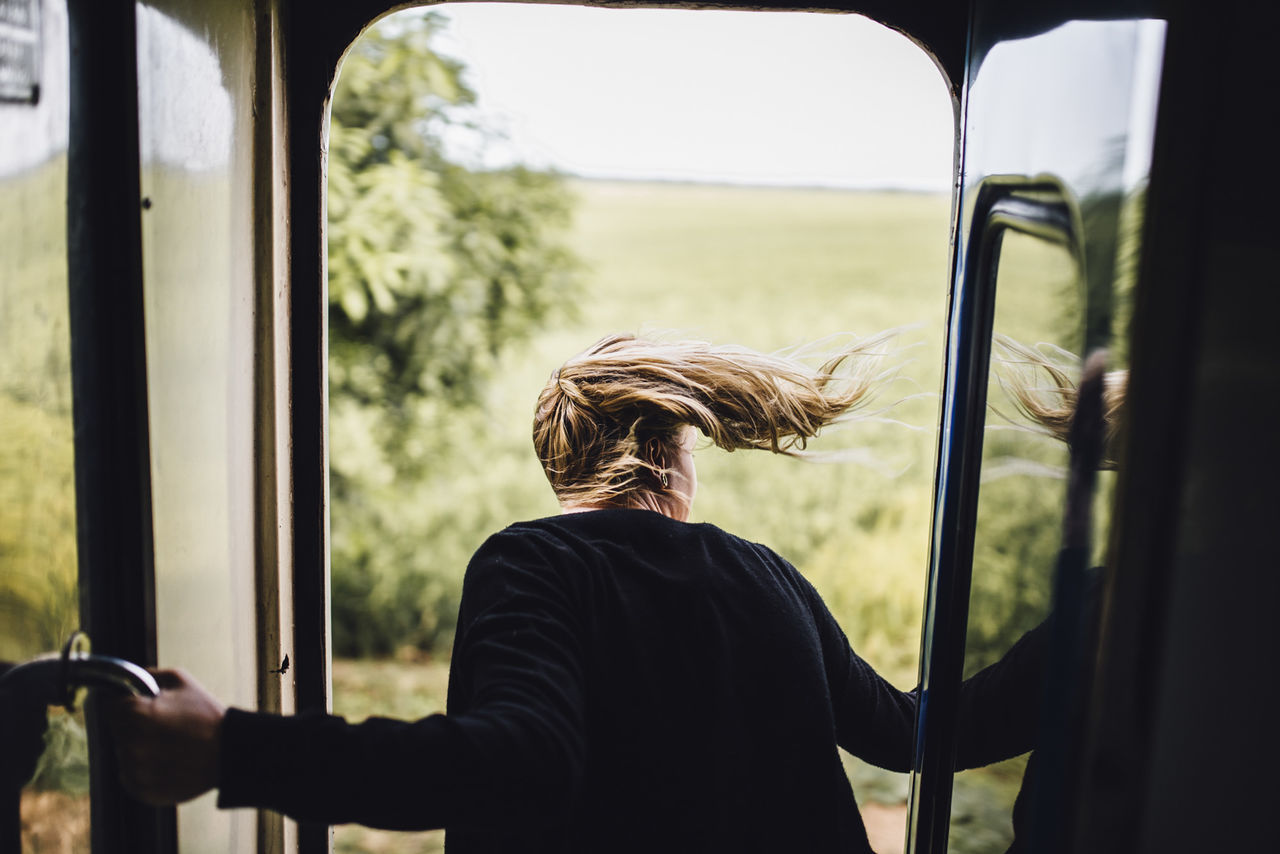 one person, adult, window, mode of transportation, transportation, black, rear view, lifestyles, travel, women, day, nature, waist up, outdoors, casual clothing, looking through window, sky, men, young adult, journey, train, land vehicle, glass, vehicle interior, person, leisure activity, bus, hairstyle, rail transportation, looking