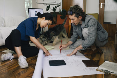 Multiracial male and female architects discussing over blueprint at home office