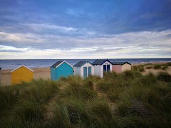 Huts on grassy beach against cloudy sky