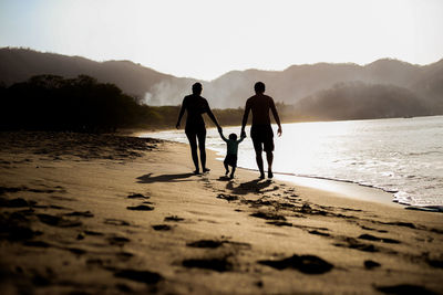 Silhouette men walking on beach against sky