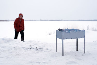 Man walking with barbeque grill on snow covered land against sky