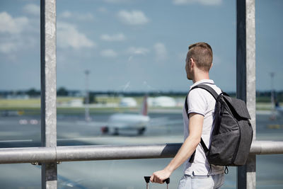 Rear view of man standing by railing against sky