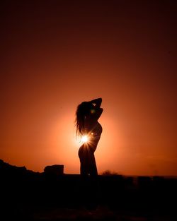 Silhouette woman standing against orange sunset sky