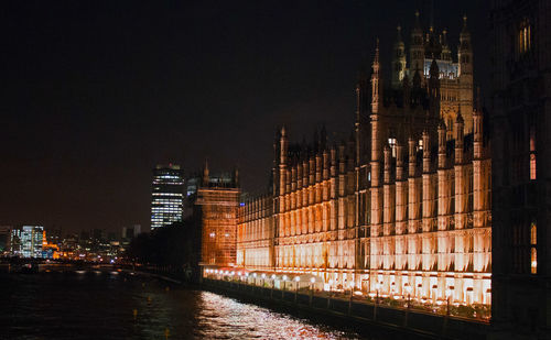 Illuminated houses of parliament by thames river against sky